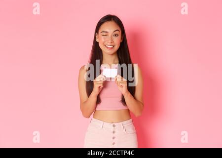 Beauté, mode et style de vie. Portrait de la fille tricherie et jolie asiatique en vêtements d'été en clin d'œil, faisant allusion à des bonus impressionnants, montrant du crédit Banque D'Images