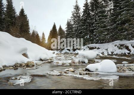 Vue à angle bas - matin sur la rivière en hiver, pierres couvertes de neige, conifères et lever le soleil à distance Banque D'Images