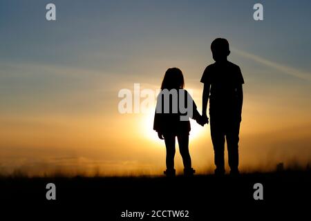 Silhouette de 2 jeunes frères et sœurs regardant le coucher du soleil Leeds Banque D'Images