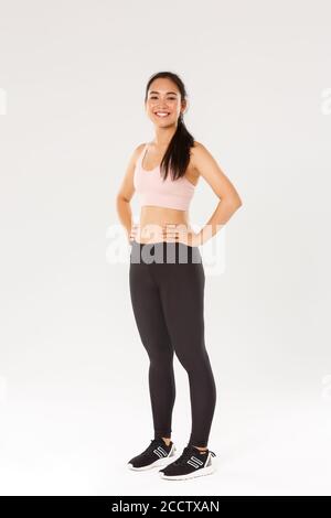 Pleine longueur de Sweaty sourire fitness fille, femme athelte en tenue active regardant heureux pendant l'entraînement, l'entraînement dans la salle de gym, satisfait avec des exercices Banque D'Images