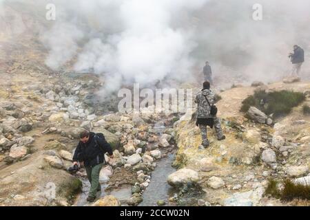 Groupe de voyageurs et de photographes se promène dans le paysage volcanique : sources chaudes, fumarale d'éruption, activité à vapeur de gaz dans le cratère du volcan actif. Banque D'Images