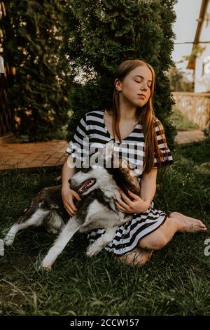 blonde fille est assis sur l'herbe verte avec un chien husky aux yeux bleus Banque D'Images