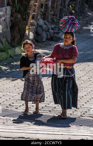 Une mère maya Cakchiquel et sa fille en robe traditionnelle portent leurs marchandises à vendre sur le marché de San Marcos la Laguna, Guatemala. Banque D'Images