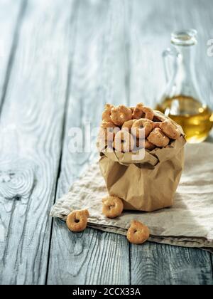 Taralli ou taralini italien traditionnel dans un sac en papier sur une ancienne table en bois grise. Photo rustique de taralli apéritif avec espace copie. Verticale Banque D'Images