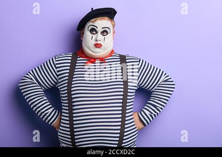 une mime épaisse et sérieuse avec un visage blanc, en regardant de côté, en tenant ses mains sur ses hanches isolées sur fond bleu. portrait en gros plan. studio shot. copy spa Banque D'Images