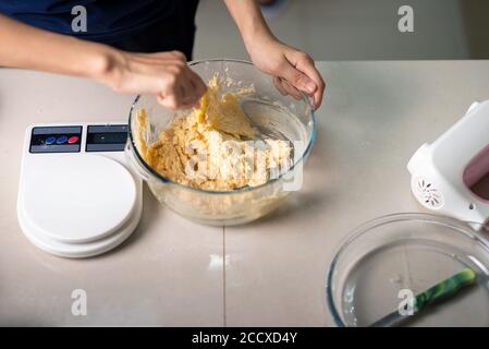 Femme mélangeant des ingrédients pour les biscuits de noix de coco pâte de sucre, les oeufs battus, le beurre et la farine pour faire des desserts faits maison dans la cuisine à la maison de gros plan Banque D'Images