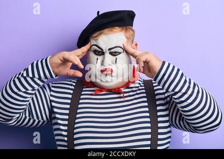 gros plan portrait d'un acteur théâtral avec un maquillage sur son visage en touchant ses temples avec les doigts. arrière-plan bleu isolé, studio tourné Banque D'Images