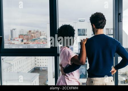 Une femme africaine positive embrasse avec son beau ami brunette européen, se détendre à la maison, se donner chaud câlin les uns aux autres, se tenir près de la fenêtre arrière-groupe Banque D'Images