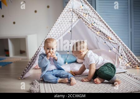 Couple de petits garçons de 1 an jouant seuls dans une tente de wigwam avec guirlande à la pépinière à l'intérieur de la maison. Banque D'Images
