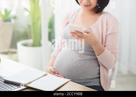 Abdomen fille travaillant avec smartphone à la table dans le bureau au troisième trimestre. Travail en ligne Banque D'Images