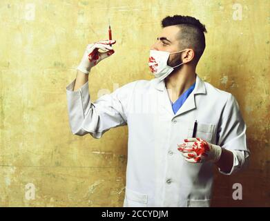 Seringue avec du sang en main par le médecin dans un masque de procédure coloré sur fond beige. Concept de traitement et d'urgence Banque D'Images