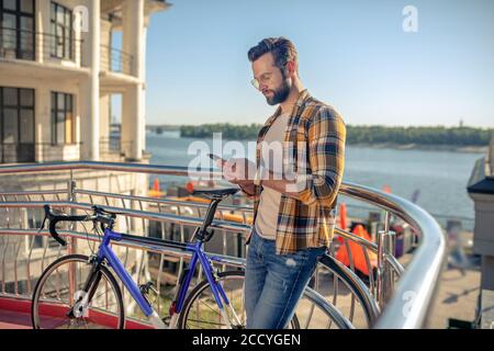 Homme regardant avec soin dans le smartphone près de la bicyclette Banque D'Images
