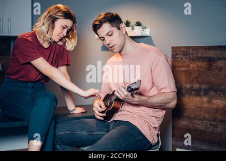 beau homme et belle femme jouant ukulele, l'homme tient ukulele dans les mains, la femme s'assoit à côté de lui profiter et écouter Banque D'Images