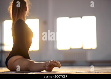 Jolie femme gracieuse est assise sur un sol clair et coloré faisant des fentes, tournant la tête vers l'arrière, regardant la fenêtre, s'étirant, se préparant pour l'activité, blu Banque D'Images