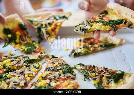 Amis qui mangent une pizza végétarienne avec des légumes dans une boîte à pizza Banque D'Images