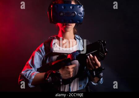 Jeune femme caucasienne tenant le tireur VR, portant un masque oculaire, se tient isolé sur fond UV Banque D'Images