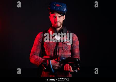 Portrait d'un jeune homme tenant une arme VR, portant une chemise décontractée, un masque sur la tête. Isolé sur fond noir Banque D'Images