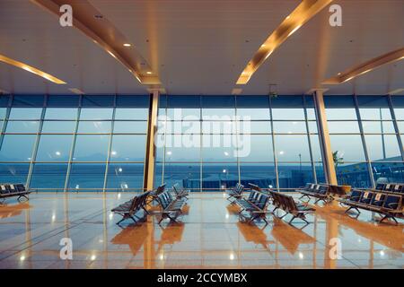 Égypte, Hurghada. Zone de départ de l'aéroport international avec sièges vides et coucher de soleil sur la piste derrière les fenêtres Banque D'Images