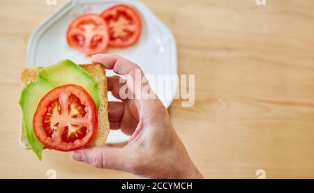 La main tient un toast frais avec de l'avocat et de la tomate comme un petit déjeuner sain Banque D'Images