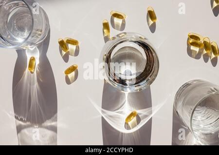 Capsules et verres Omega 3 avec de l'eau sur une table blanche. Banque D'Images