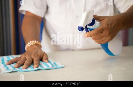 Gros plan des mains désinfection de la table à l'aide d'un assainisseur - nettoyage de la poussière sur la surface du bureau à l'aide d'un chiffon et d'un vaporisateur désinfectant, pour protéger du coronavirus Banque D'Images