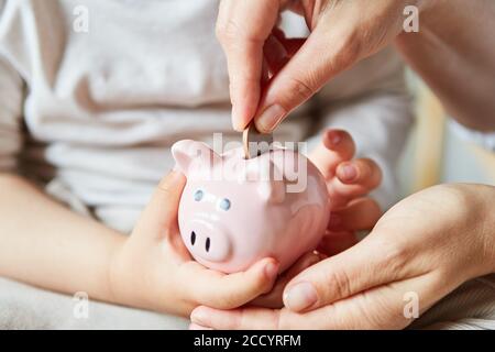 Main met une pièce dans la banque de porc rose de un enfant Banque D'Images