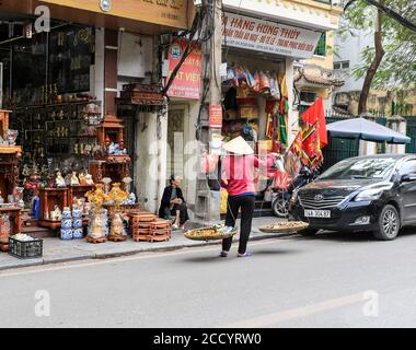 Un commerçant ou un vendeur de rue portant un chapeau conique vietnamien (nón lá) vendant des fruits et des noix, Hanoi, Vietnam, Asie Banque D'Images