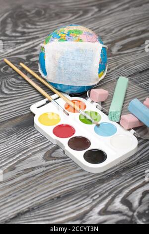 Globe avec masque médical. À proximité se trouvent des crayons et des aquarelles. Année académique pendant l'épidémie. Banque D'Images