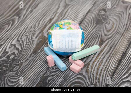 Globe avec masque médical. À proximité sont des crayons. Année académique pendant l'épidémie. Banque D'Images