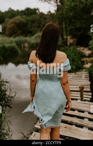 brunette fille dans une robe turquoise marche à travers la rivière seul un vieux pont en bois Banque D'Images