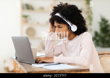 Fille adolescente noire à l'ordinateur portable étudiant en ligne assis à la maison Banque D'Images
