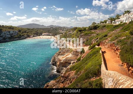 Scène typique de plage espagnole avec chemin menant à la plage entourée de collines verdoyantes et de montagnes avec ciel bleu, Cala Romantica, Mallorcal, Espagne. Banque D'Images