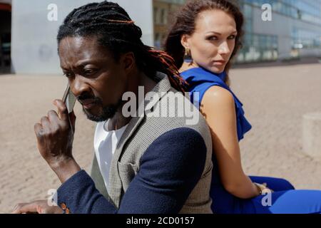 Homme africain et femme européenne de race blanche sur une promenade dans la ville, homme parlant au téléphone. Jour d'été. Photo de haute qualité Banque D'Images