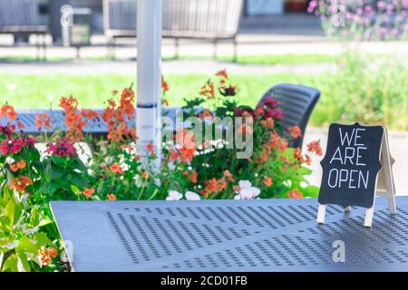 Tableau noir avec inscription NOUS SOMMES OUVERTS sur la table dans le café de la ville. Panneau CAFEV Open manuscrit en ville invitant les clients. Tables et chaises de restaurant Banque D'Images