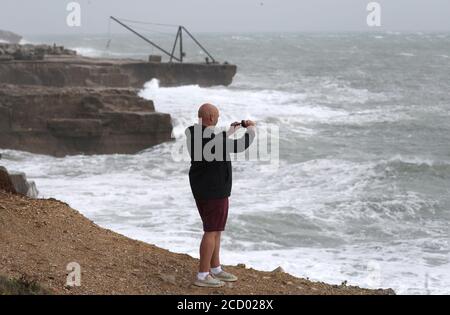 Une personne prend une photo du bord de la falaise alors que les vagues s'écrasont contre le rivage à Portland Bill à Dorset. Banque D'Images