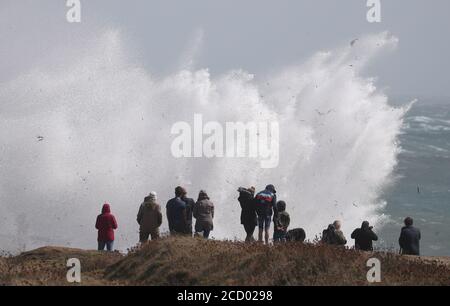 Les gens se tiennent à côté d'un trou de soufflage alors que les vagues s'écrasent contre le rivage à Portland Bill à Dorset. Banque D'Images