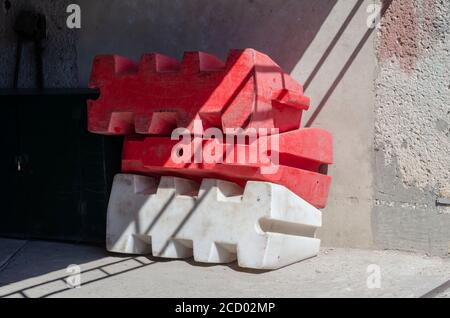 Les barrières en plastique remplies d'eau de la route sont empilées contre le mur. Deux clôtures de sécurité rouges et une clôture blanche. Sécurité. Mise au point sélective. Banque D'Images