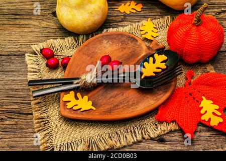 Réglage de la table d'automne. Thanksgiving ou Halloween concept. Assiette en céramique en forme de feuilles, couverts noirs, citrouilles et baies de rosé pour chiens. Anciennes planches de bois ba Banque D'Images