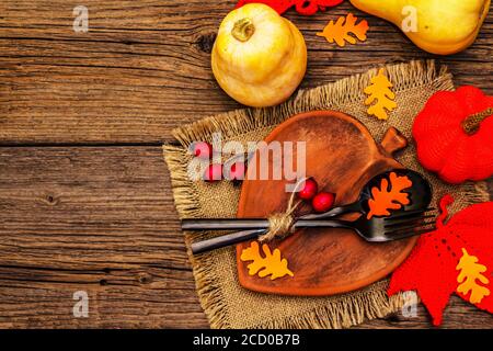 Réglage de la table d'automne. Thanksgiving ou Halloween concept. Assiette en céramique en forme de feuilles, couverts noirs, citrouilles et baies de rosé pour chiens. Anciennes planches de bois ba Banque D'Images