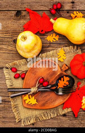 Réglage de la table d'automne. Thanksgiving ou Halloween concept. Assiette en céramique en forme de feuilles, couverts noirs, citrouilles et baies de rosé pour chiens. Anciennes planches de bois ba Banque D'Images