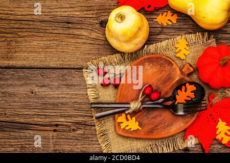 Réglage de la table d'automne. Thanksgiving ou Halloween concept. Assiette en céramique en forme de feuilles, couverts noirs, citrouilles et baies de rosé pour chiens. Anciennes planches de bois ba Banque D'Images