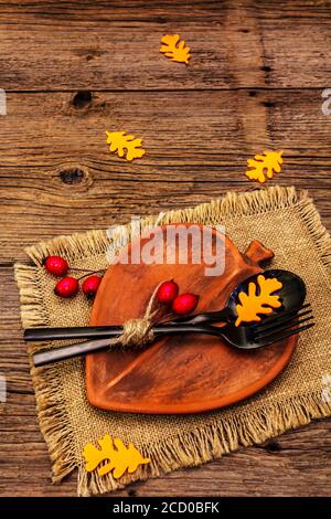Réglage de la table d'automne. Thanksgiving ou Halloween concept. Assiette en céramique en forme de feuilles, couverts noirs, citrouilles et baies de rosé pour chiens. Anciennes planches de bois ba Banque D'Images