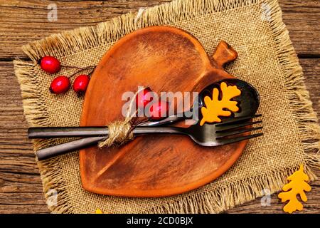 Réglage de la table d'automne. Thanksgiving ou Halloween concept. Assiette en céramique en forme de feuilles, couverts noirs, citrouilles et baies de rosé pour chiens. Anciennes planches de bois ba Banque D'Images