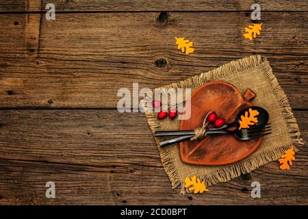 Réglage de la table d'automne. Thanksgiving ou Halloween concept. Assiette en céramique en forme de feuilles, couverts noirs, citrouilles et baies de rosé pour chiens. Anciennes planches de bois ba Banque D'Images