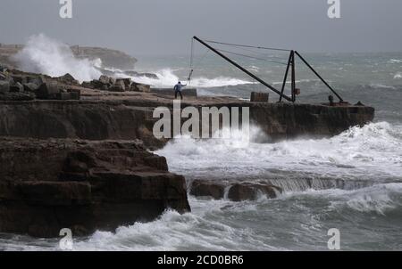 Un homme regarde les vagues s'écraser contre le rivage à Portland Bill à Dorset. Banque D'Images