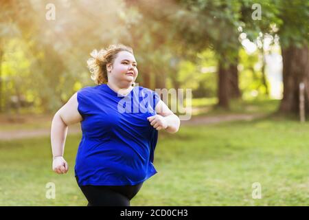Une jeune blonde de taille plus fait du jogging dans le parc lors d'une soirée ensoleillée d'été. Concept de mode de vie sain Banque D'Images