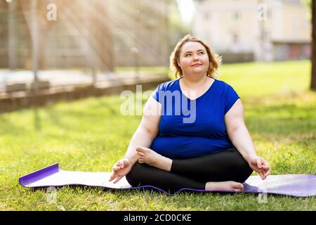 Jeune blond de taille plus médite sur un tapis de gymnastique lors d'une soirée ensoleillée d'été. Concept de mode de vie sain Banque D'Images