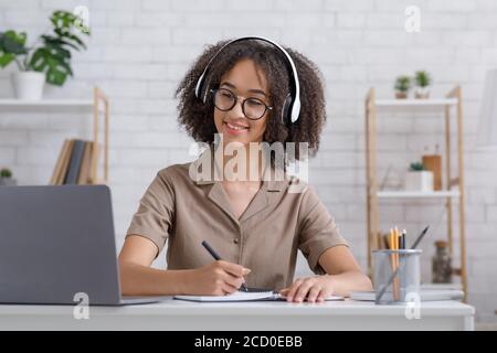 Restez à la maison et étudiez en ligne. Une petite fille sympathique prend des notes dans un ordinateur portable et écoute le séminaire en ligne sur un ordinateur portable Banque D'Images