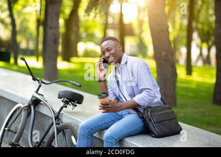 Homme afro-américain confiant avec vélo et café en conversation sur téléphone portable au parking Banque D'Images