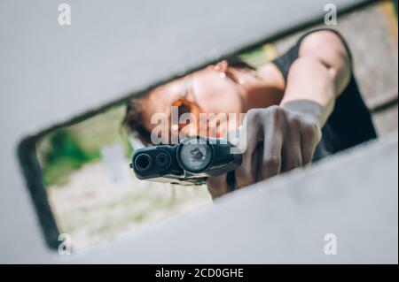 Vue rapprochée et abstraite d'un soldat de l'armée féminin attirante. Entraînement de tir à l'arme à feu de derrière et autour de la couverture ou de la barricade. Tacti de combat avancé Banque D'Images